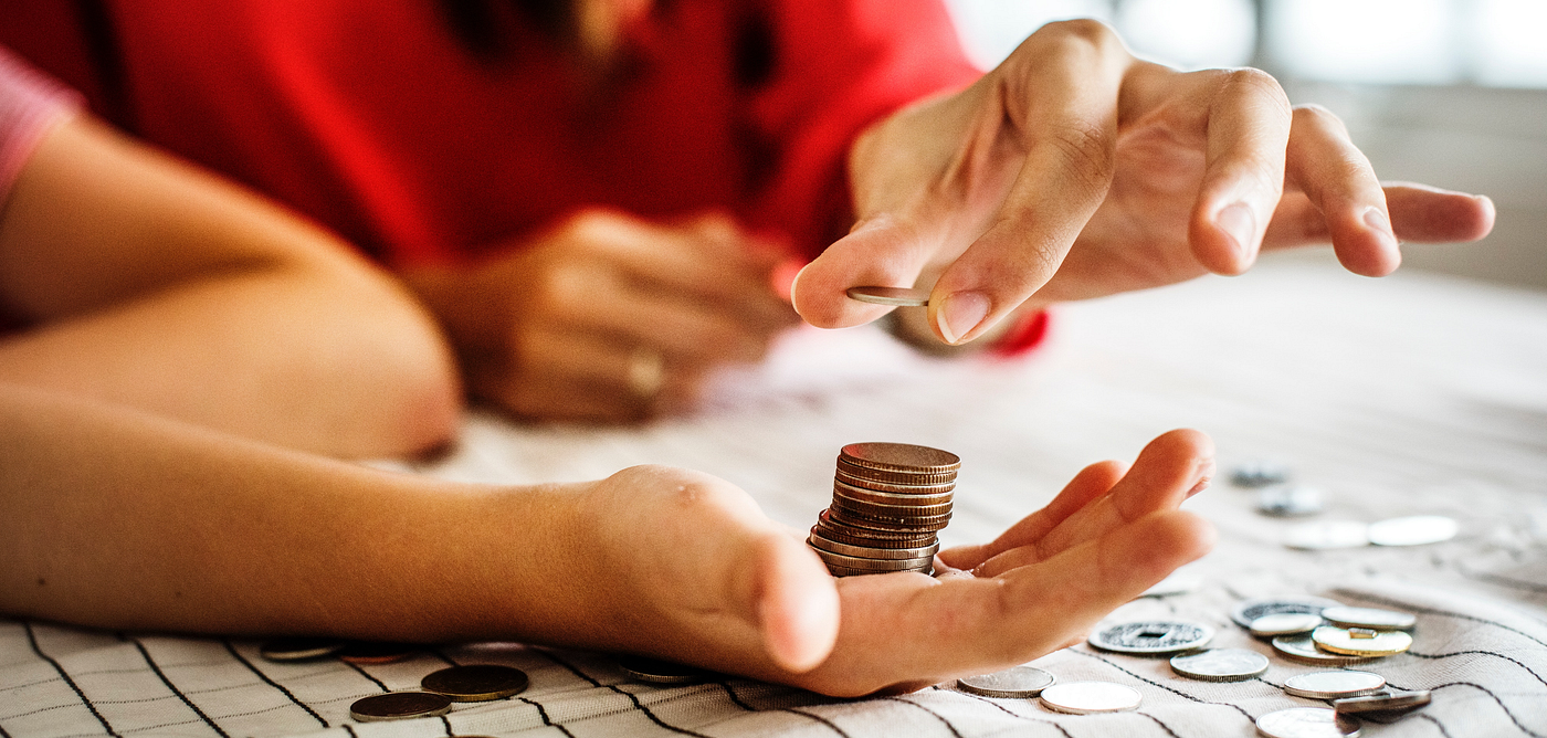A photo of someone placing a pile of coins on someone else’s palm.